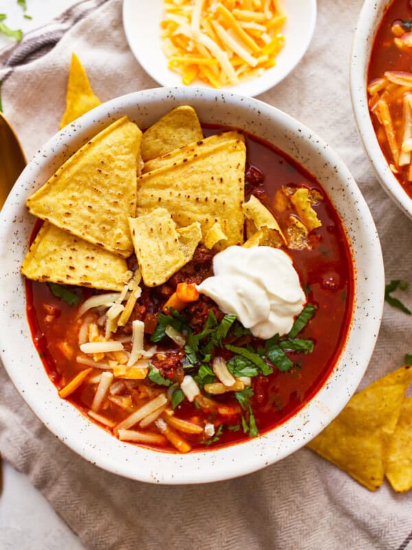 Two bowls of mexican chili soup with sour cream and tortilla chips.