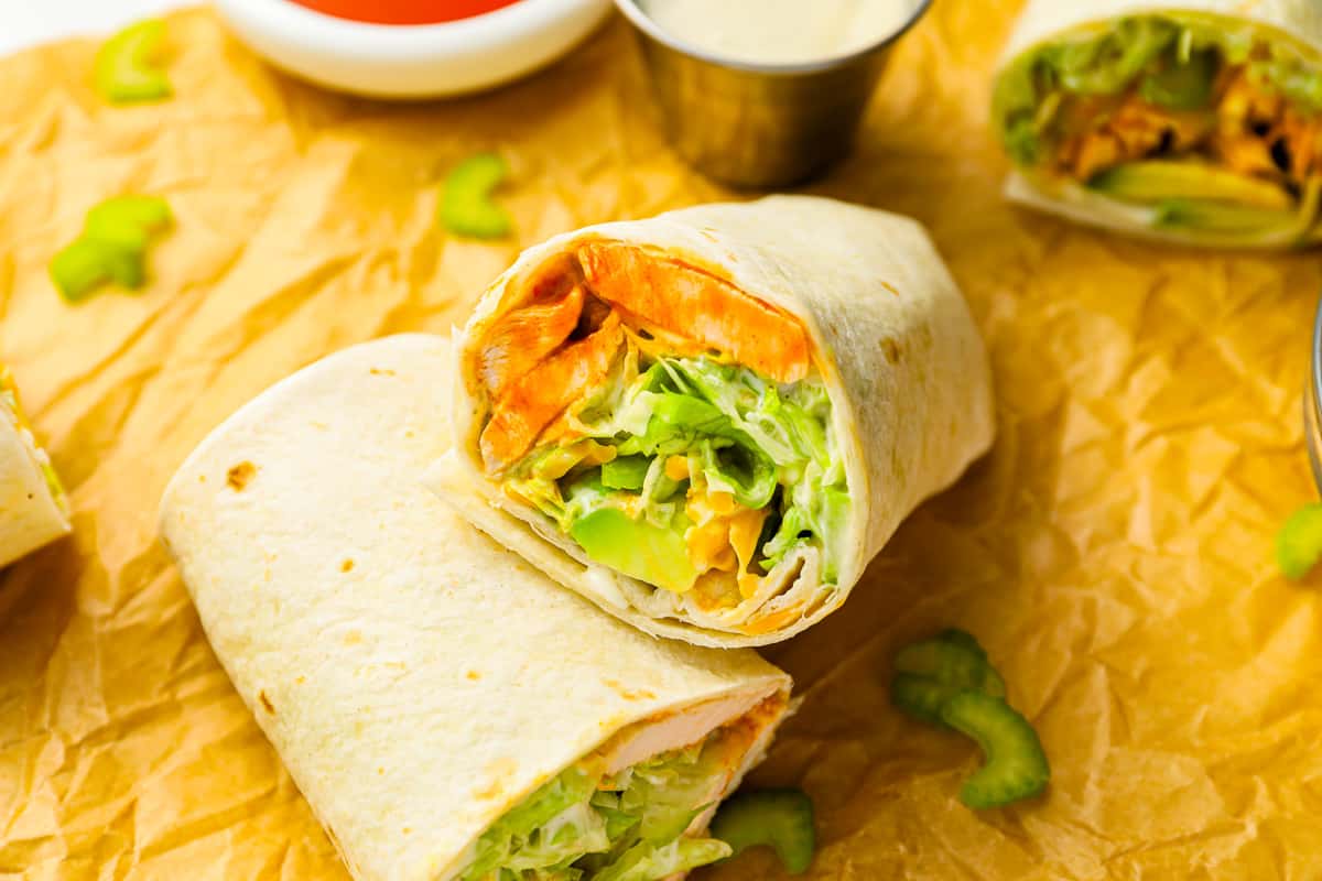 Buffalo chicken wraps with vegetables and sauce on a piece of paper.