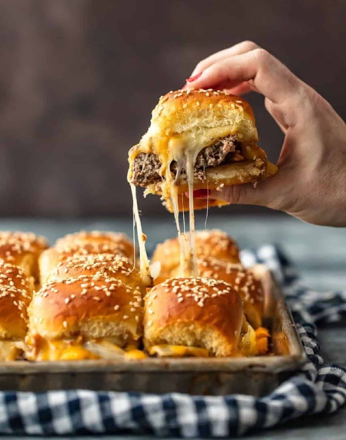 Cheeseburger Sliders are a fun and easy meal perfect for those busy school nights or fun game days! There’s nothing better than this EASY Pull Apart Baked Cheeseburger Slider Recipe for feeding a hungry crowd. So much cheese, so little time! hand lifting up cheeseburger slider