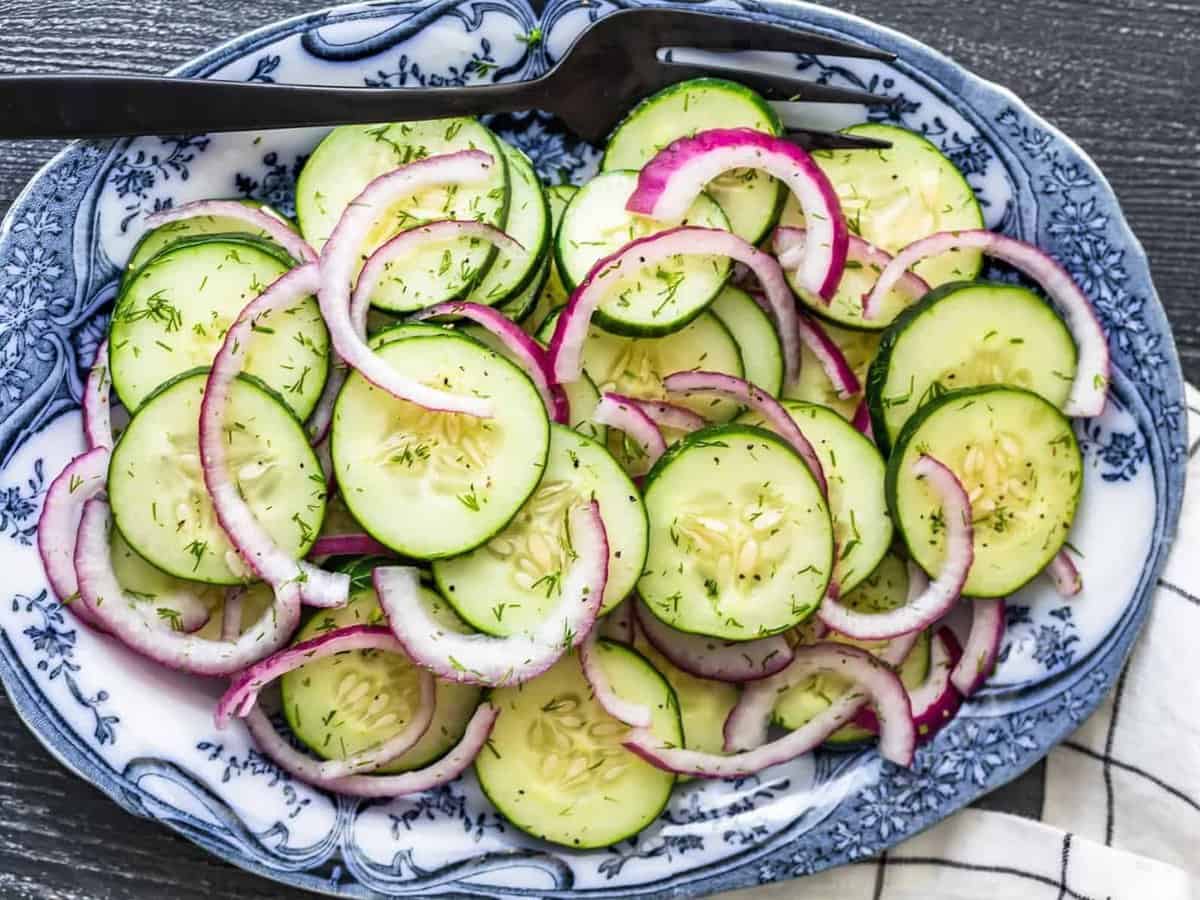 overhead view of cucumber salad with red onions and vinegar dressing, on a white and blue serving plater