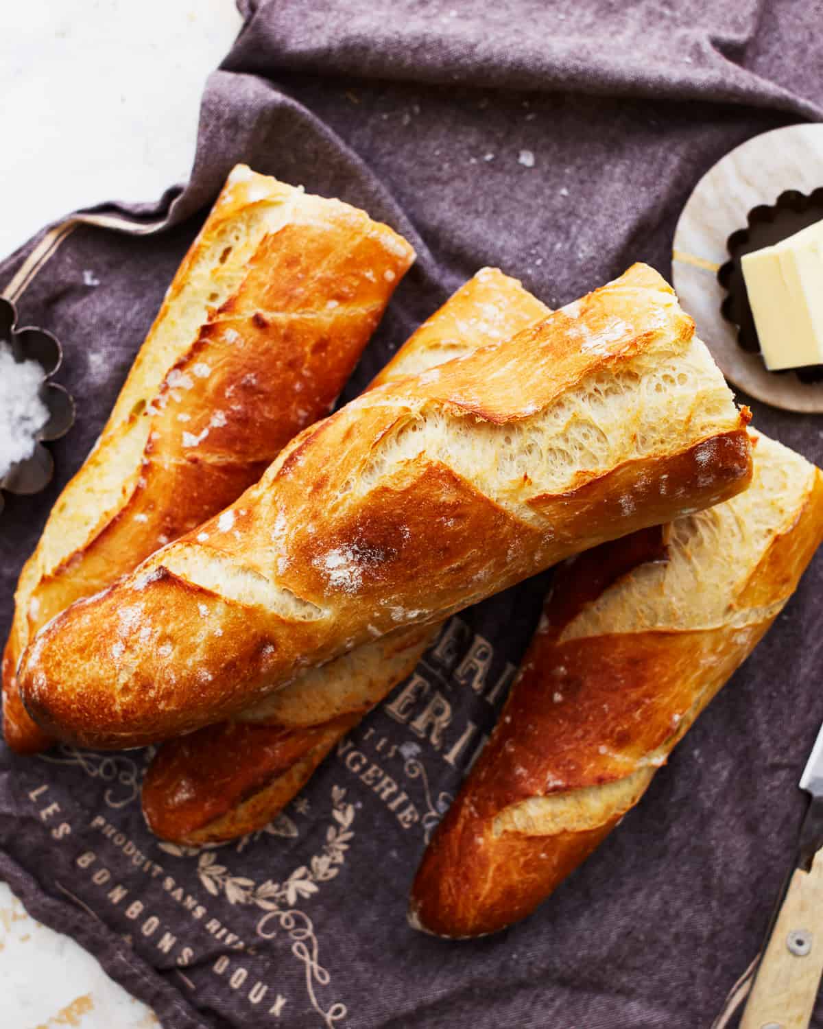 A bunch of french baguettes on a table with butter and a knife.