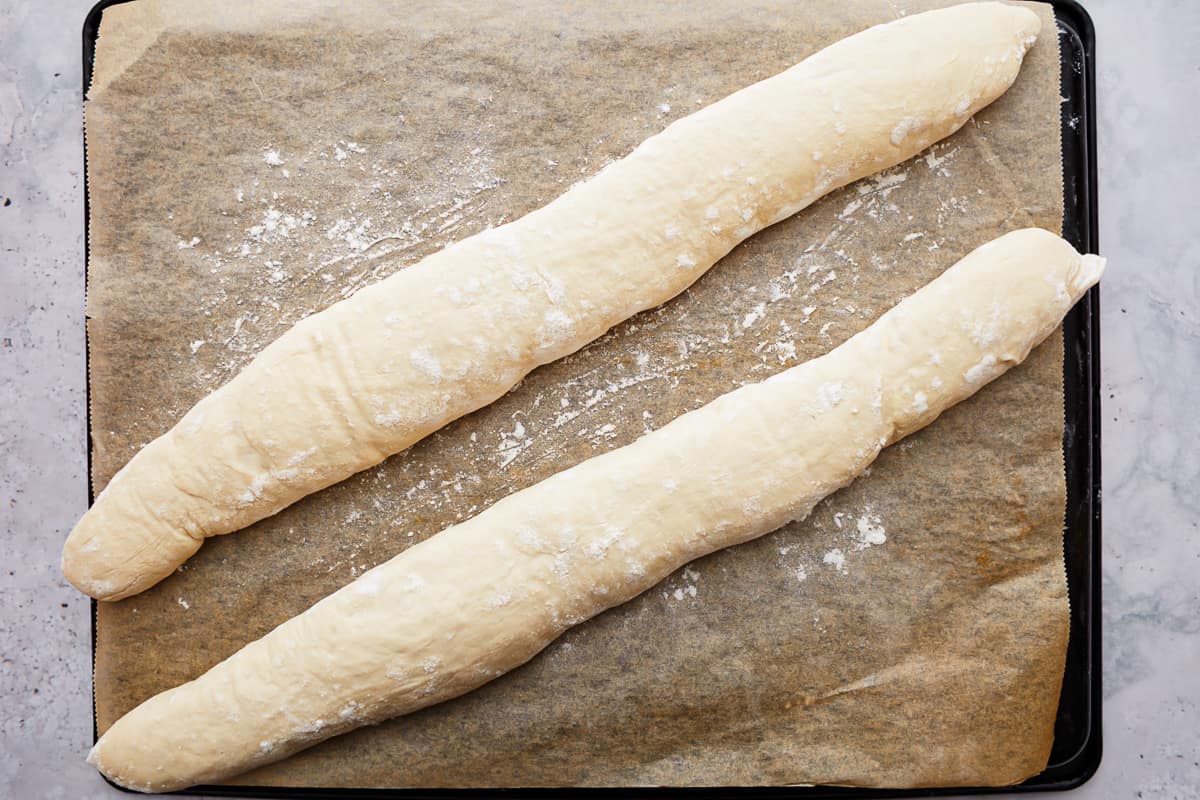 Shaped baguette dough on a parchment-lined baking tray.