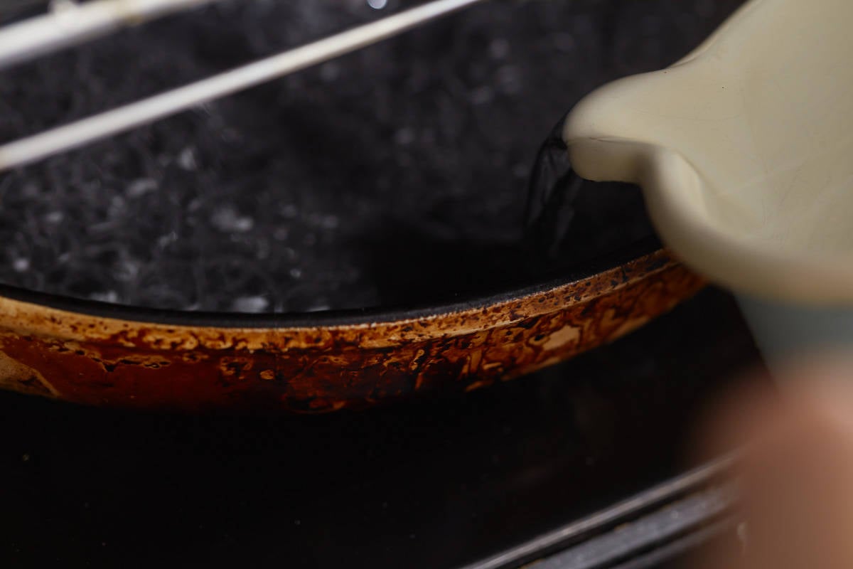 Pouring water into a pan in the oven to create steam.