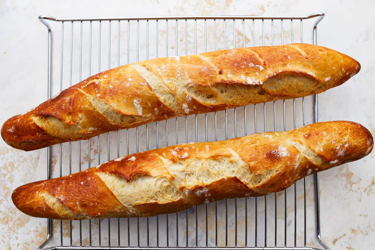 Two fresh-baked French baguettes on a cooling rack.