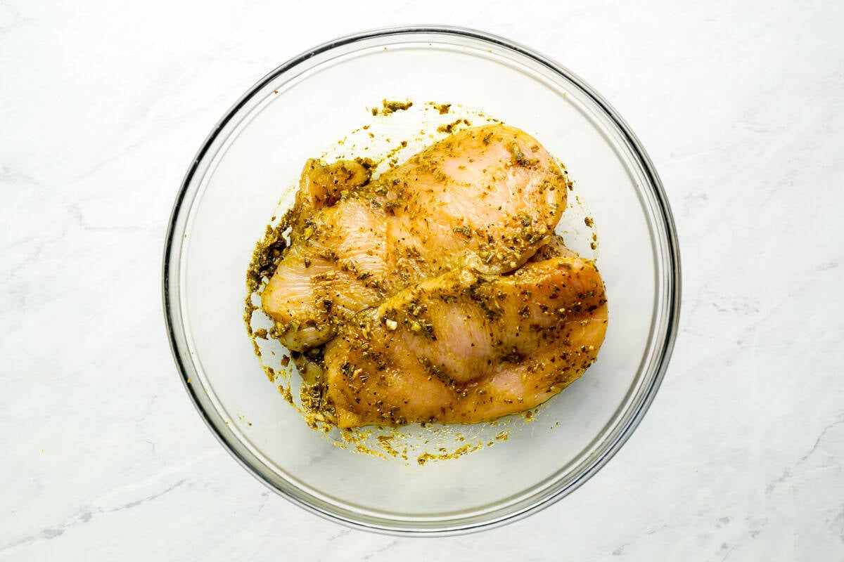 chicken breasts coated in pesto in a glass bowl.